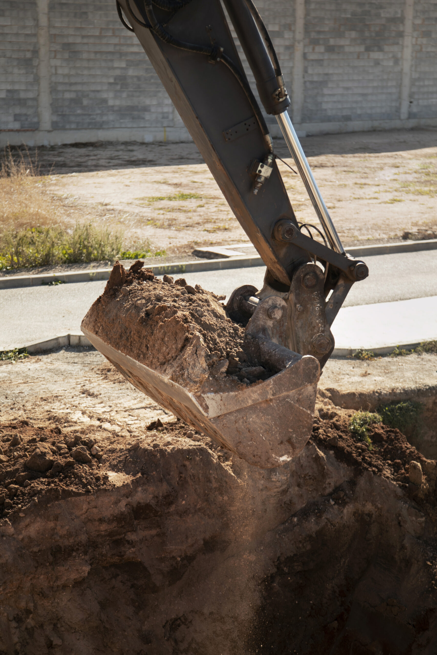 Excavator bucket dropping dirt into an open trench.