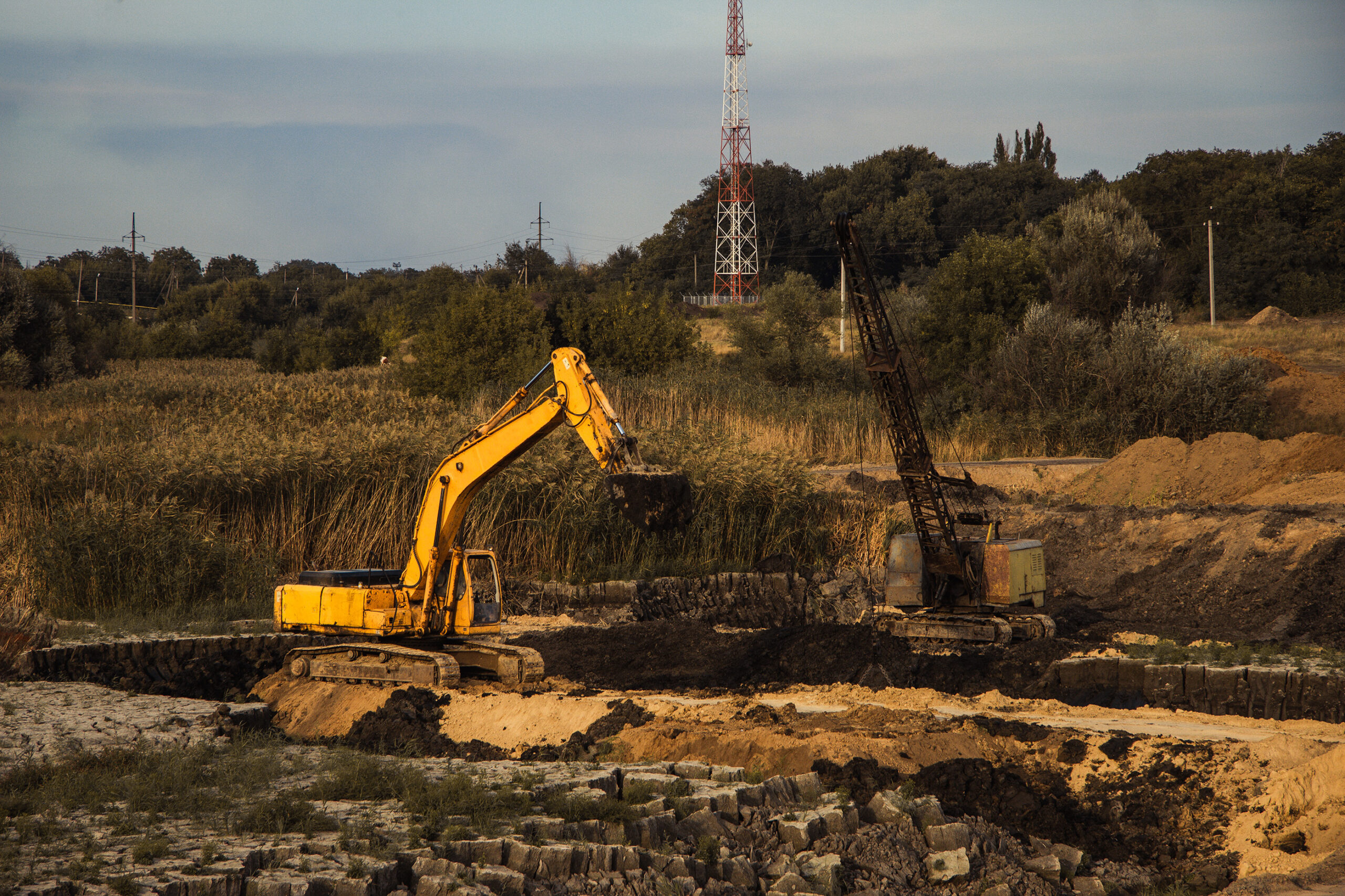 Yellow excavator and crane digging at a rural site.