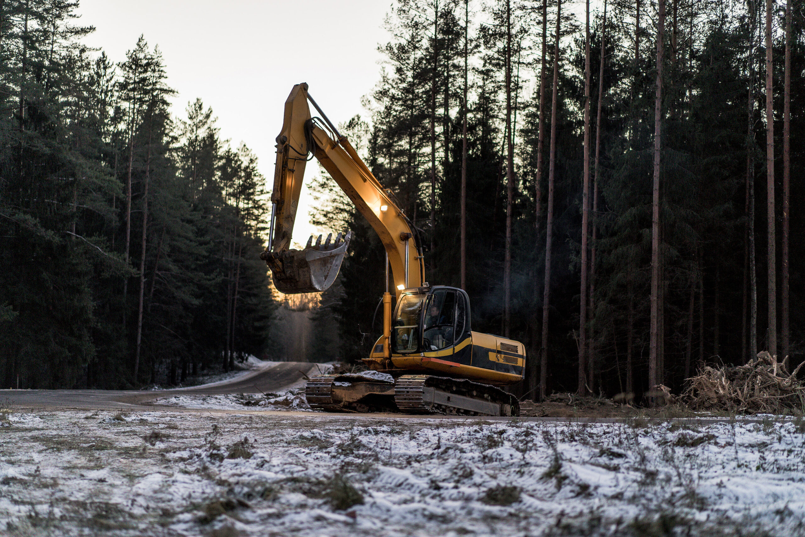 Yellow excavator parked on a snowy road by a forest.