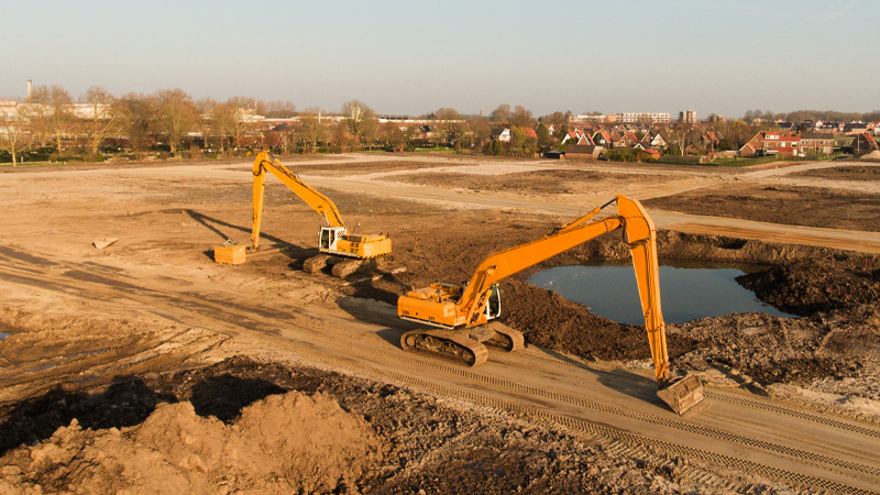 Two orange excavators on a large dirt construction site.