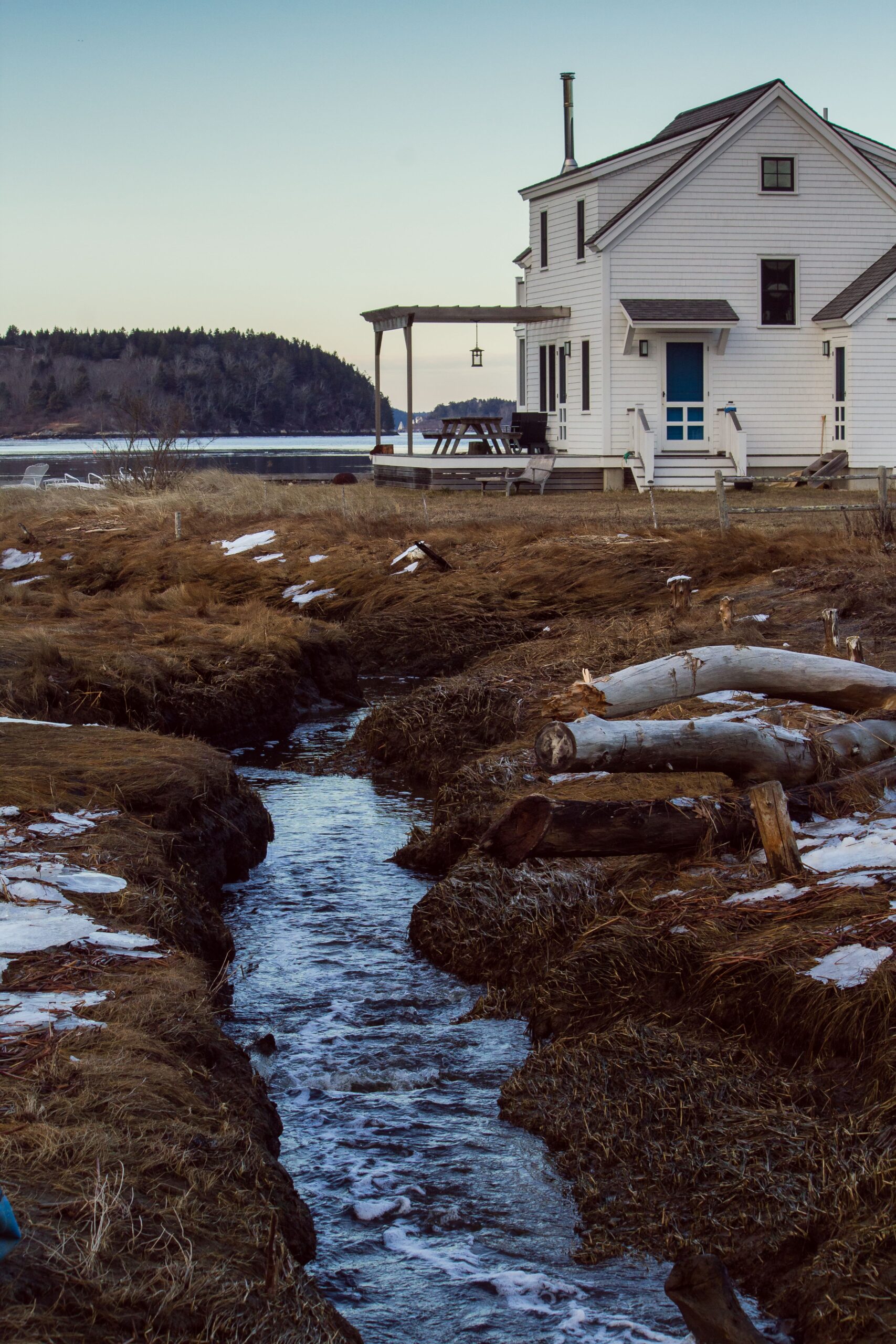 White house by a stream with a view of a forested hill.
