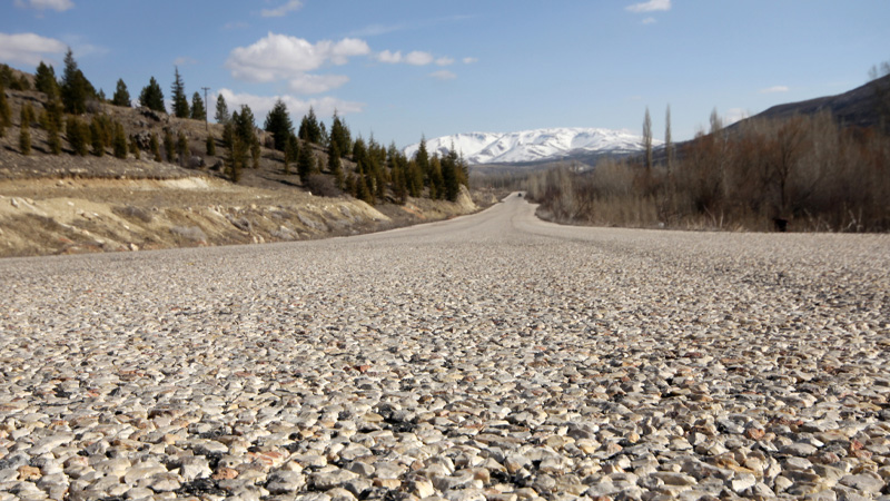 Low-angle view of a gravel road leading to snowy mountains.