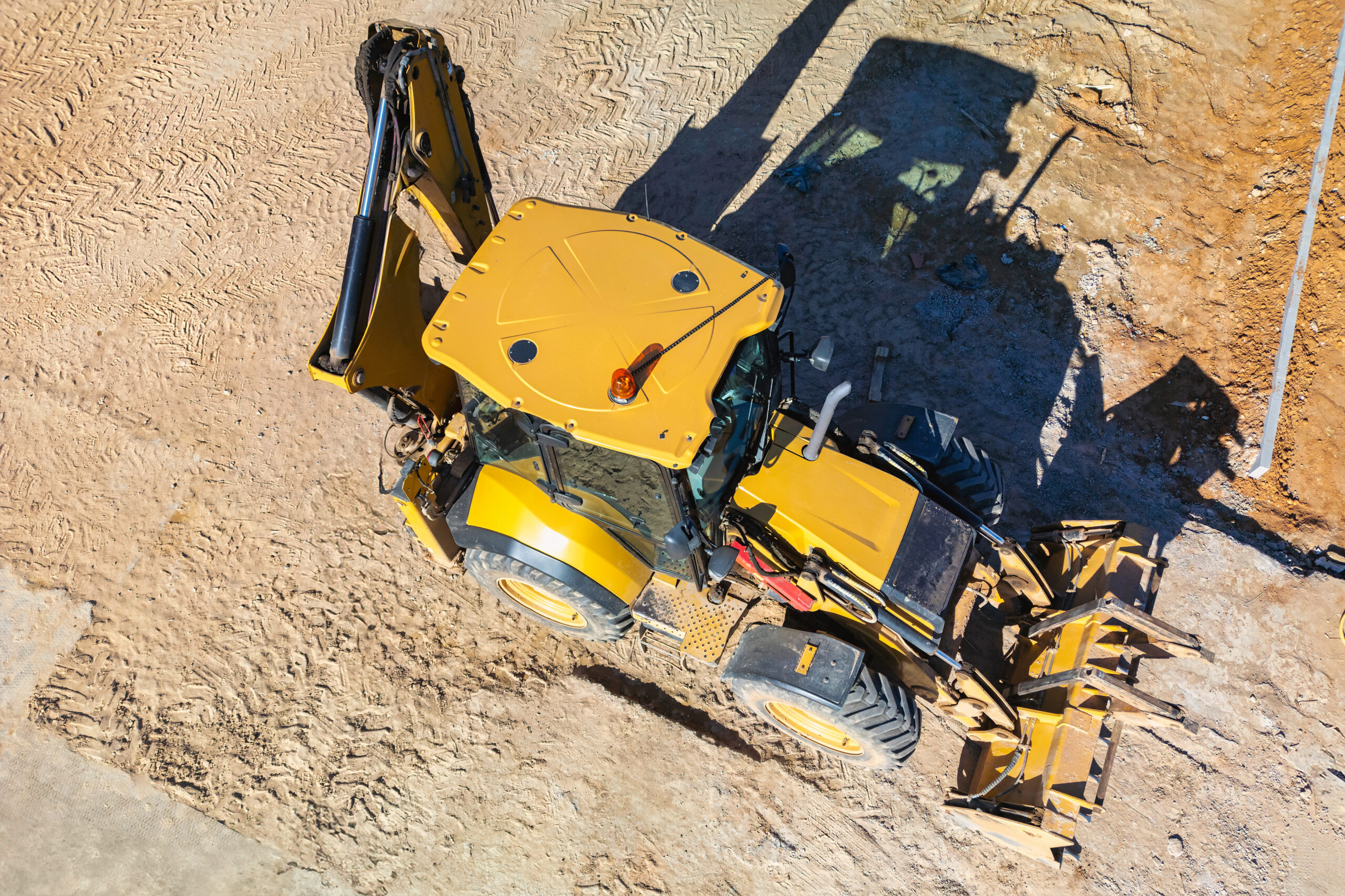 Aerial view of a yellow backhoe on a dirt construction site.